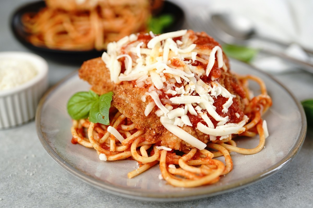 Chicken Parmesan, mit Spaghetti serviert, auf einem grauen Teller.