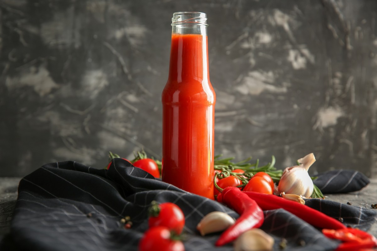 Flasche mit Chilisoße, Chilis, Knoblauch und Tomaten daneben.