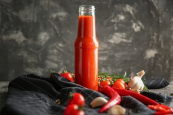 Flasche mit Chilisoße, Chilis, Knoblauch und Tomaten daneben.