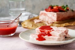 Zwei Scheiben Erdbeer-Parfait mit Fruchtpüree auf einem Teller.