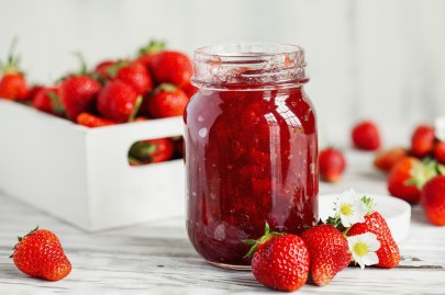 Erdbeermarmelade selber machen: Ein Glas Erdbeermarmelade, daneben und dahinterliegen frische Erdbeeren.