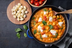 Pfanne mit Gnocchi in Tomatensahnesoße mit Burrata, Brett mit Gnocchi und Tomaten daneben.