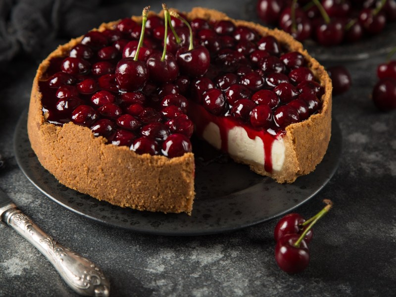 Ein angeschnittener und dekorierter Kirsch-Käsekuchen.