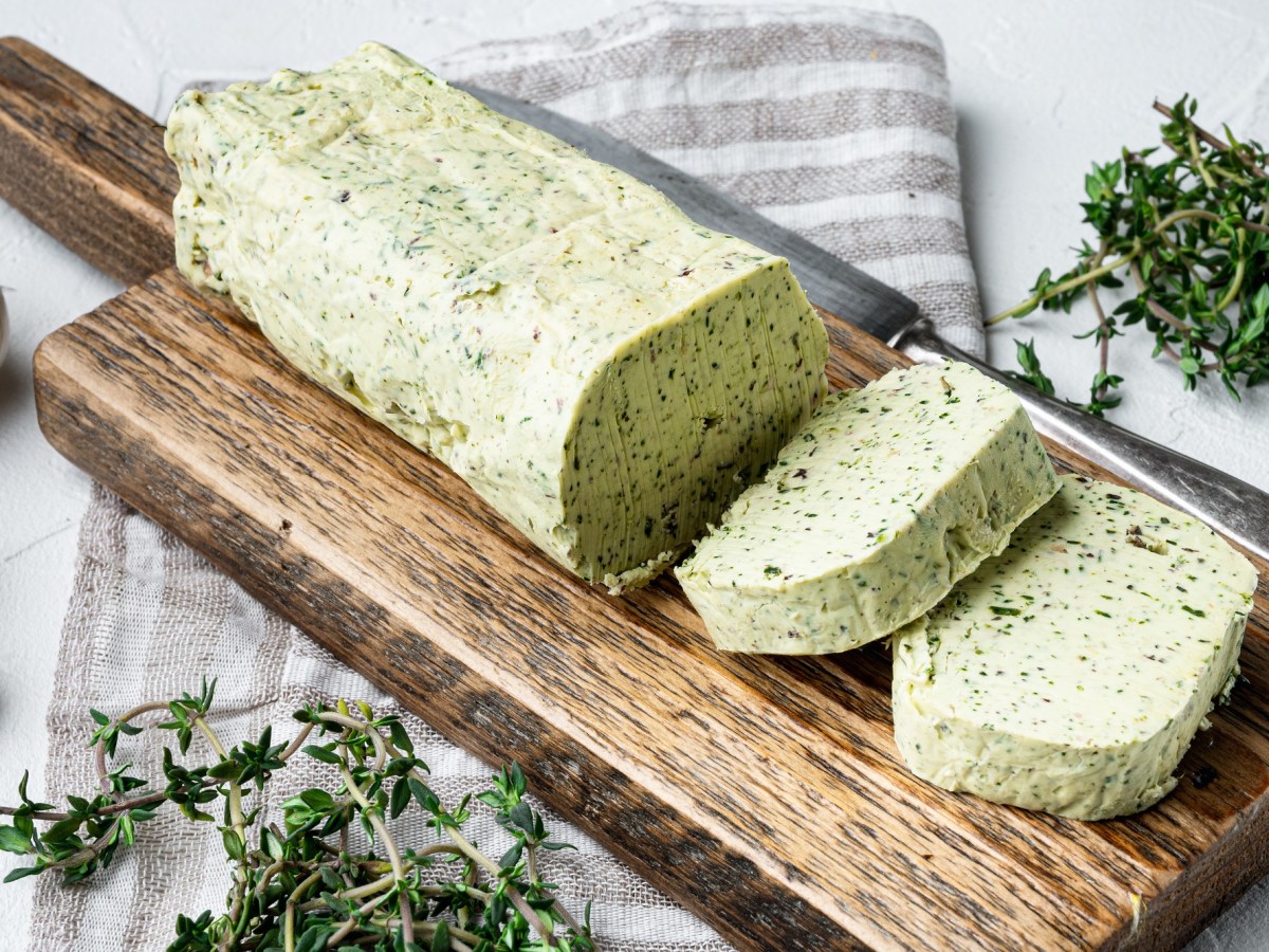 Kräuterbutter selber machen: Eine angeschnittene Rolle Kräuterbutter liegt auf einem Holzbrett.