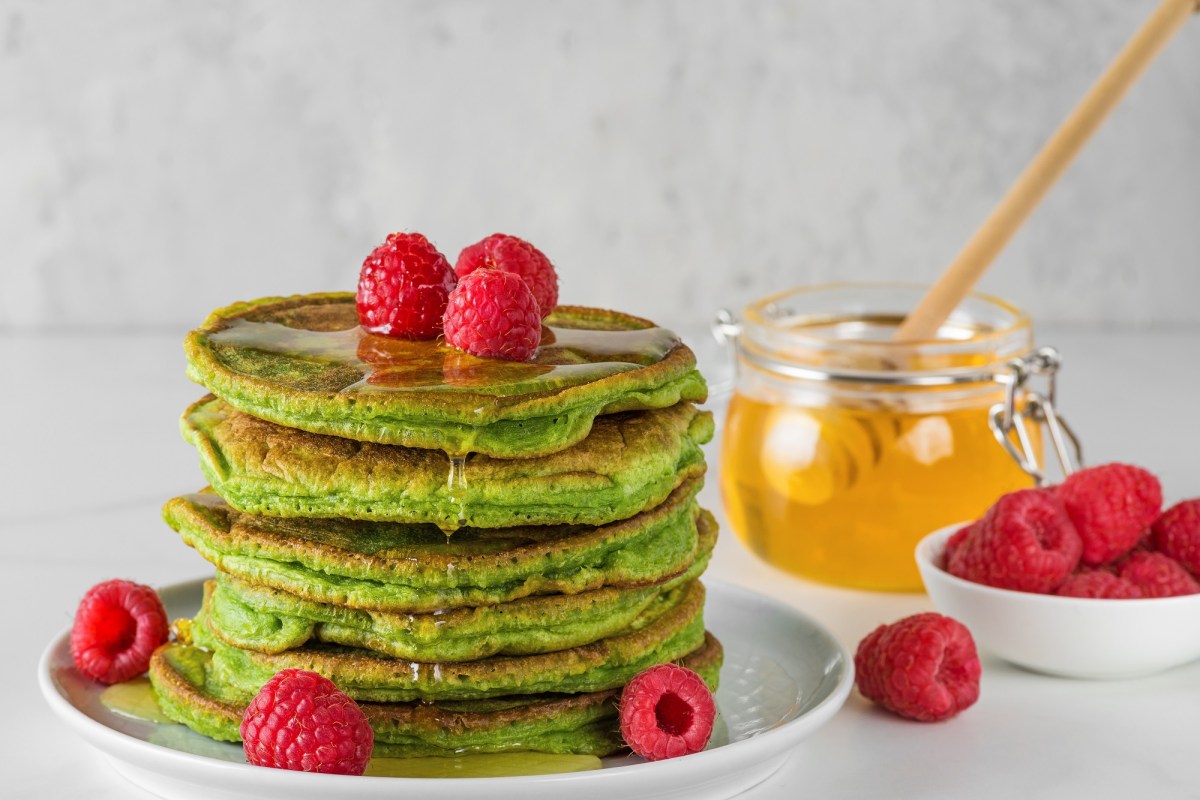 Ein Stapel Matcha-Pancakes. Garniert sind sie mit Honig und frischen Himbeeren.