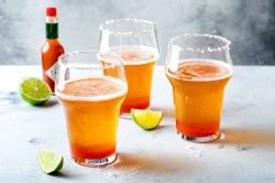 Drei Gläser mit Michelada, Flasche mit Chilisoße und Limettenspalten.