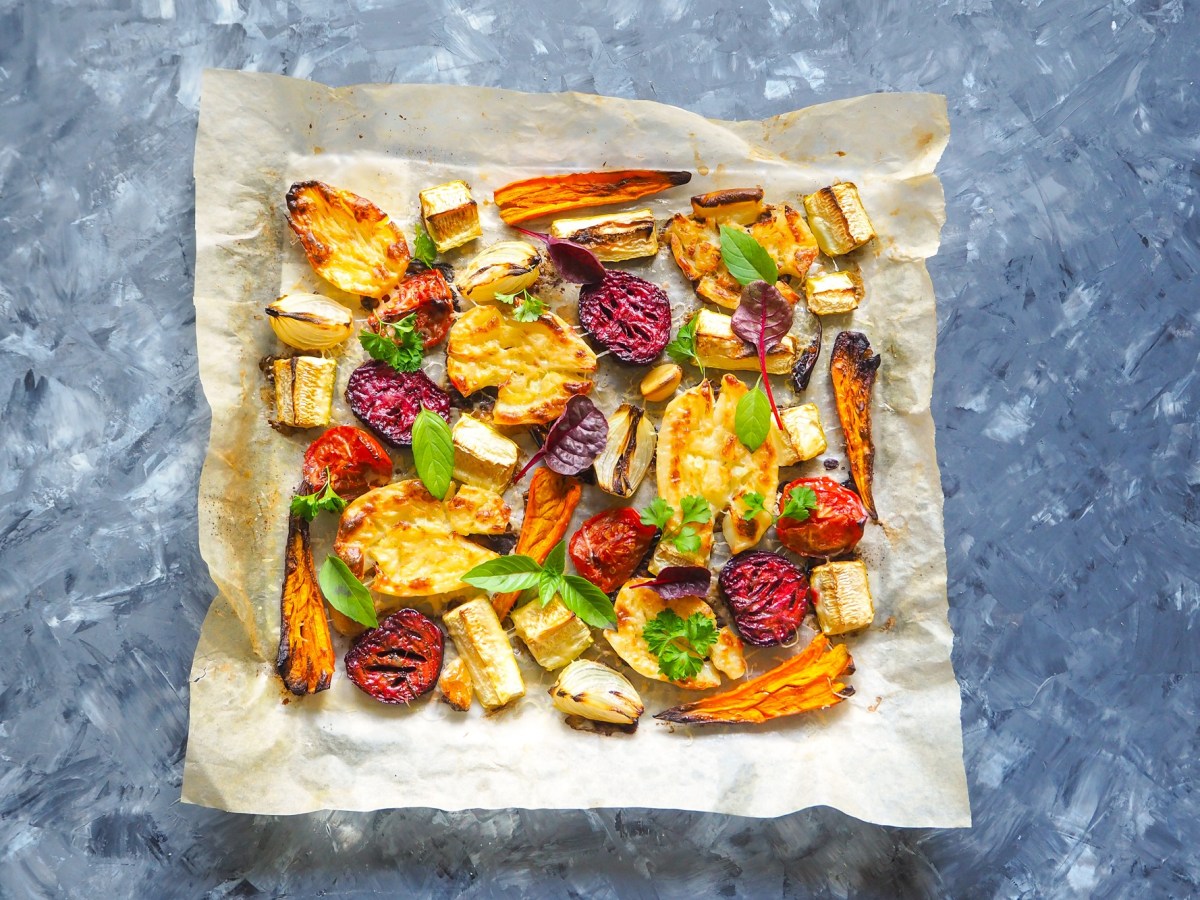 Ofengemüse mit Halloumi auf einem Blech. Dieses steht auf einem blauen Hintergrund.