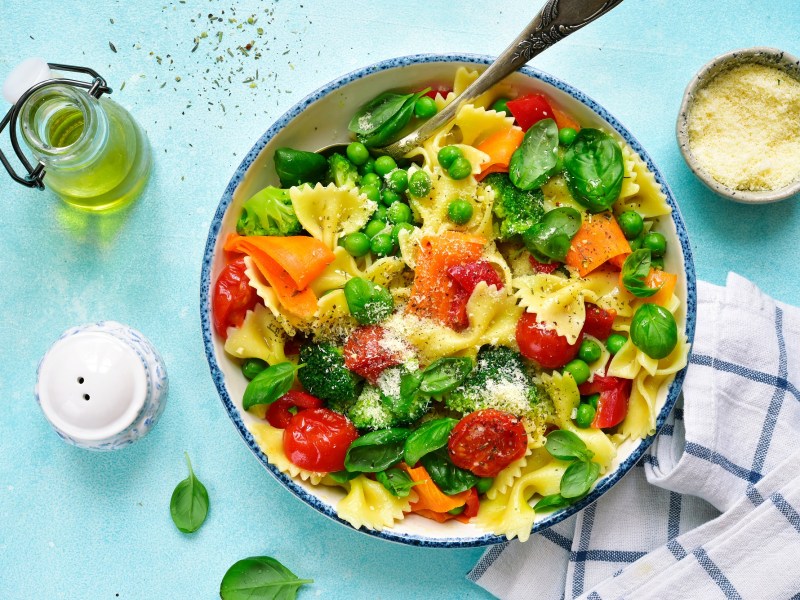 Teller mit Pasta Primavera auf blauem Untergrund