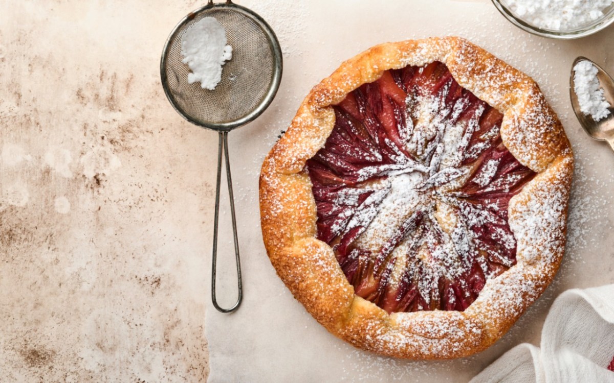 Eine Rhabarber-Galette mit Puderzucker in der Draufsicht. Daneben liegt ein Sieb mit Puderzucker.