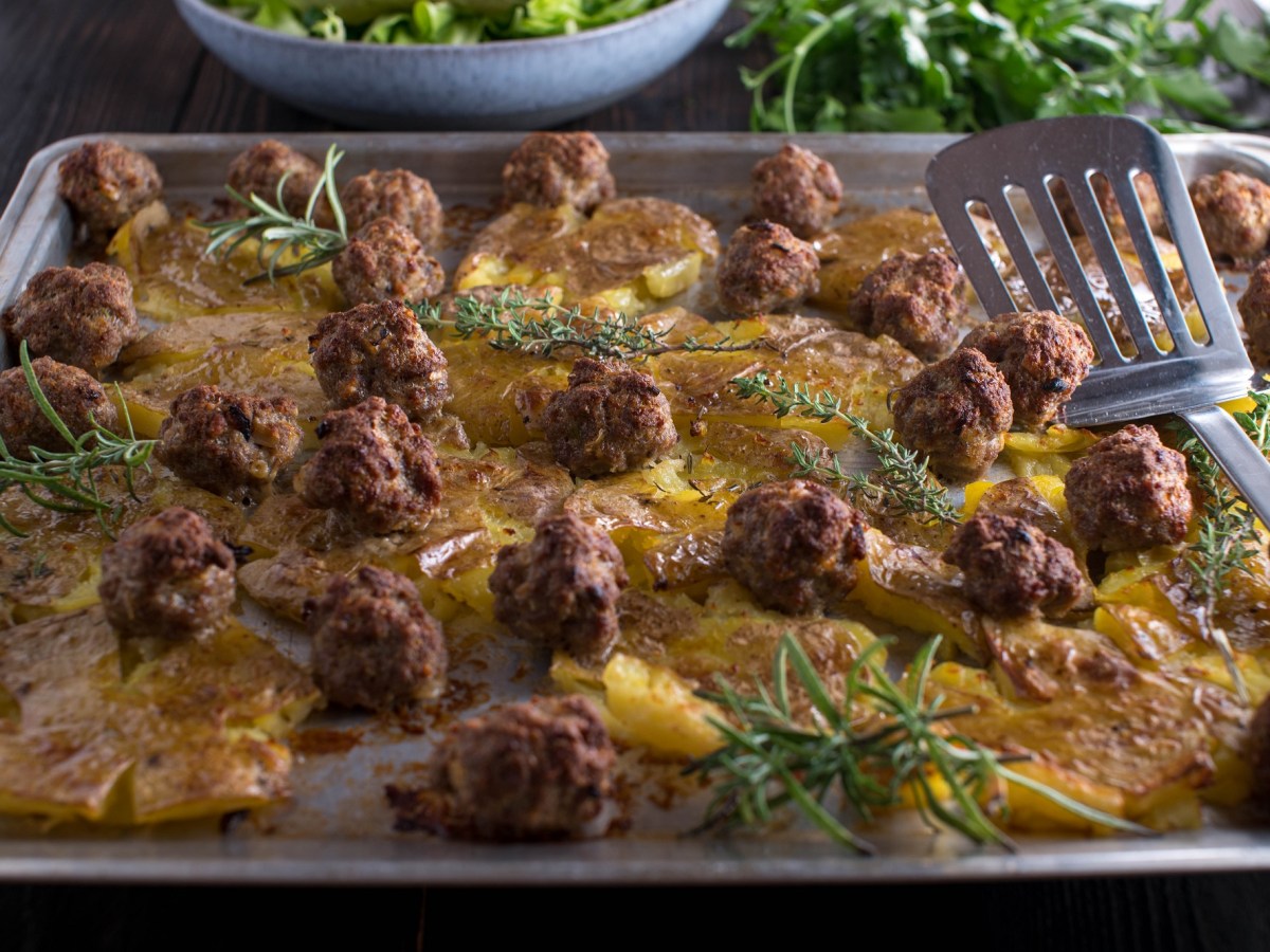 Ein Backblech mit Smashed Potatoes mit Bouletten.