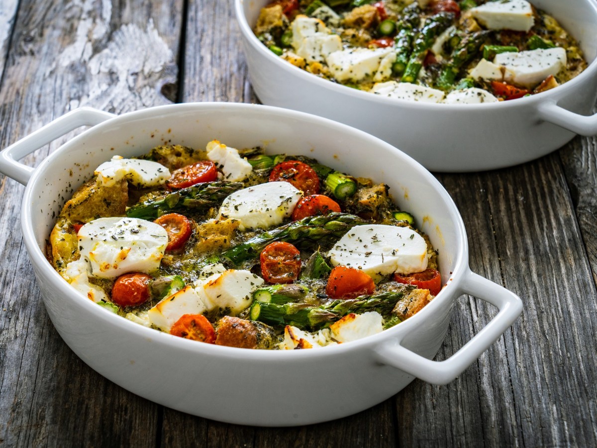 zwei Auflaufformen mit Spargel-Feta-Auflauf mit Kartoffeln und Tomaten.