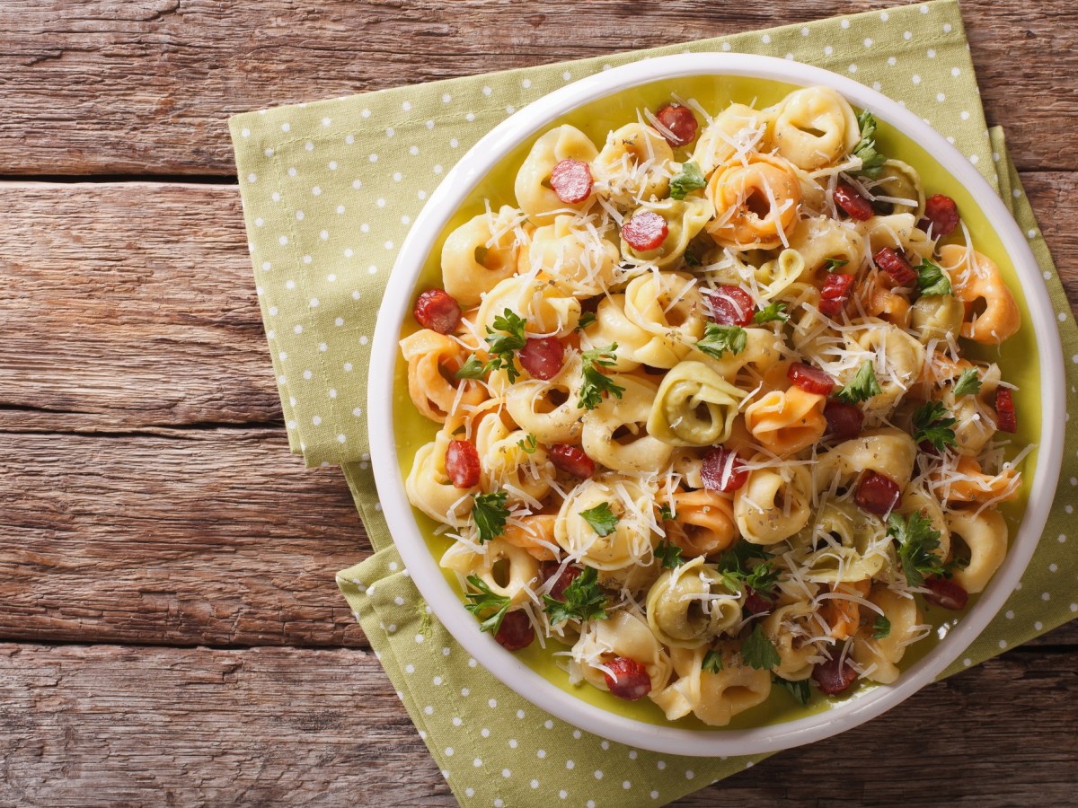 Tortellini-Salat mit Salami in einer weißen Schüssel auf einer Stoffserviette