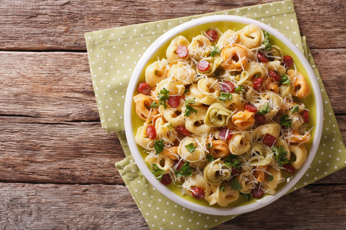 Tortellini-Salat mit Salami in einer weißen Schüssel auf einer Stoffserviette