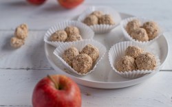 Mehrere Portionen Apfel-Energy-Balls auf einem Teller. Daneben liegen Äpfel.