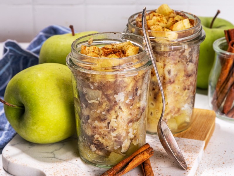 Apfelkuchen im Glas mit Äpfeln, Zimt und blauem Geschirrtuch.