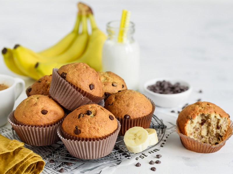 Mehrere Bananen-Muffins auf einem Kuchengitter, Bananen daneben