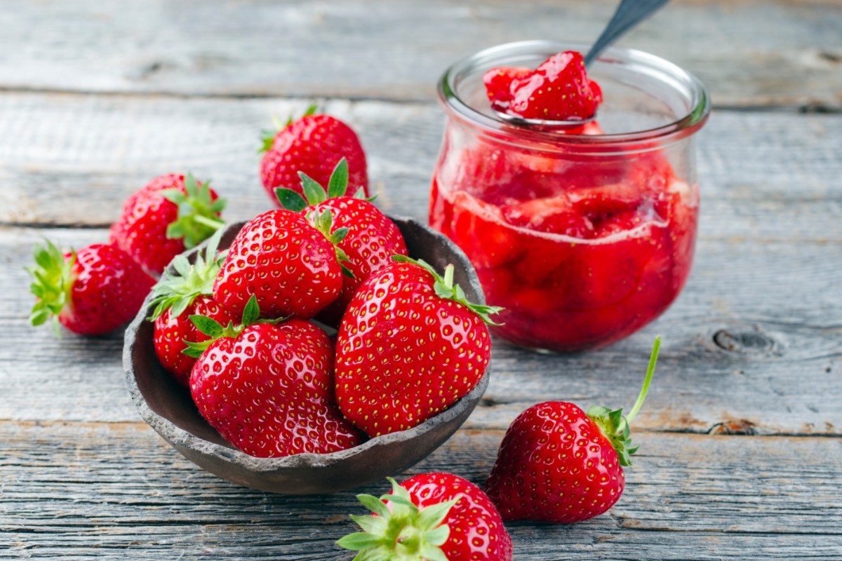 Ein Glas Erdbeerkompott, daneben frische Erdbeeren.