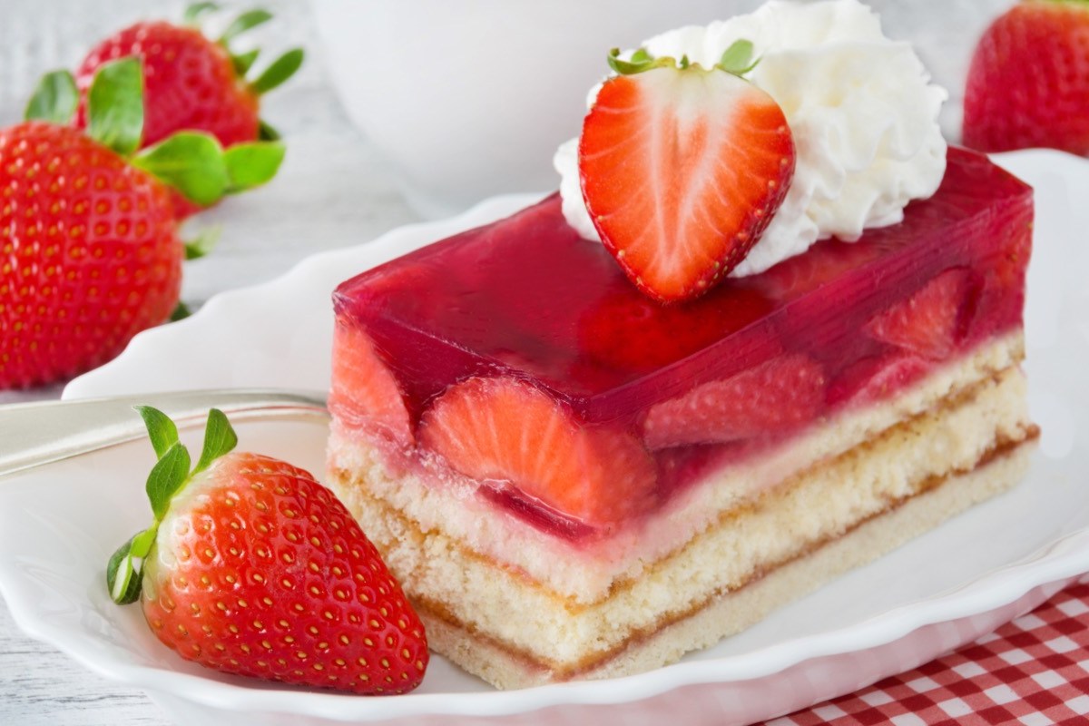 Eine Erdbeerschnitte auf einem Teller, dekoriert mit frischen Erdbeeren und Sahne.