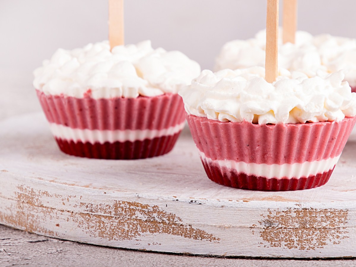 3 Frozen-Yogurt-Muffins garniert mit Sahnetupfen auf einem Brett.