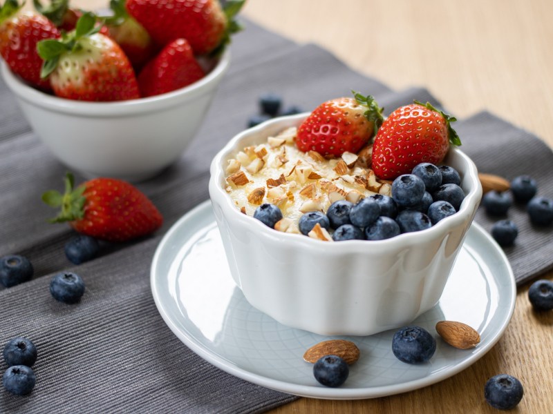 eine Schüssel Grießpudding mit Erdbeeren, Blaubeeren und gehackten Mandeln, daneben eine Schüssel Erdbeeren.