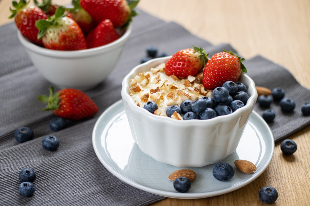 eine Schüssel Grießpudding mit Erdbeeren, Blaubeeren und gehackten Mandeln, daneben eine Schüssel Erdbeeren.