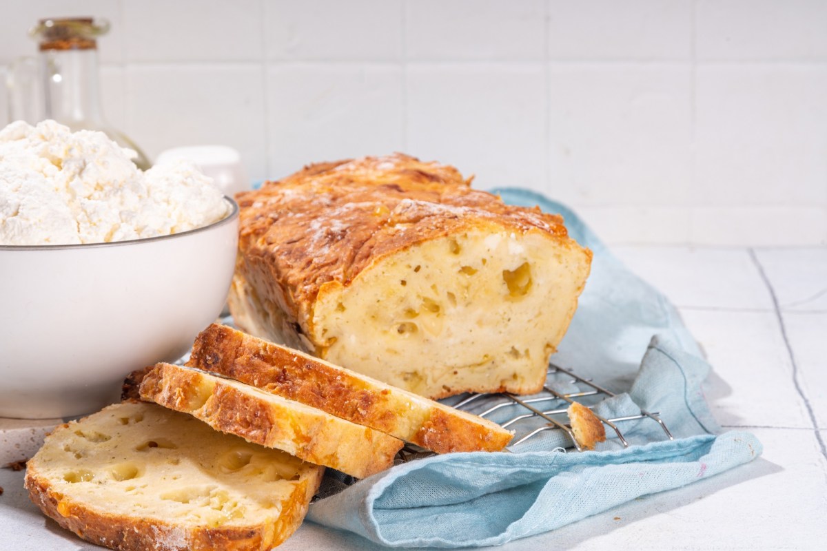 Angeschnittenes Hüttenkäse-Brot auf einer blauen Serviette. Daneben steht eine Schüssel mit Hüttenkäse.