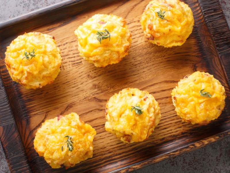 Sechs Käse-Kartoffel-Muffins auf einem Holztablett, in der Draufsicht.