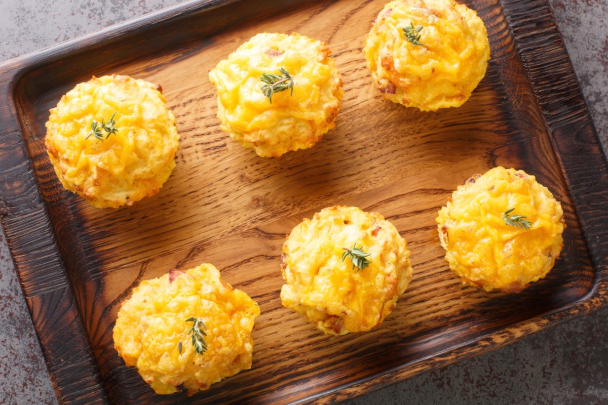 Sechs Käse-Kartoffel-Muffins auf einem Holztablett, in der Draufsicht.