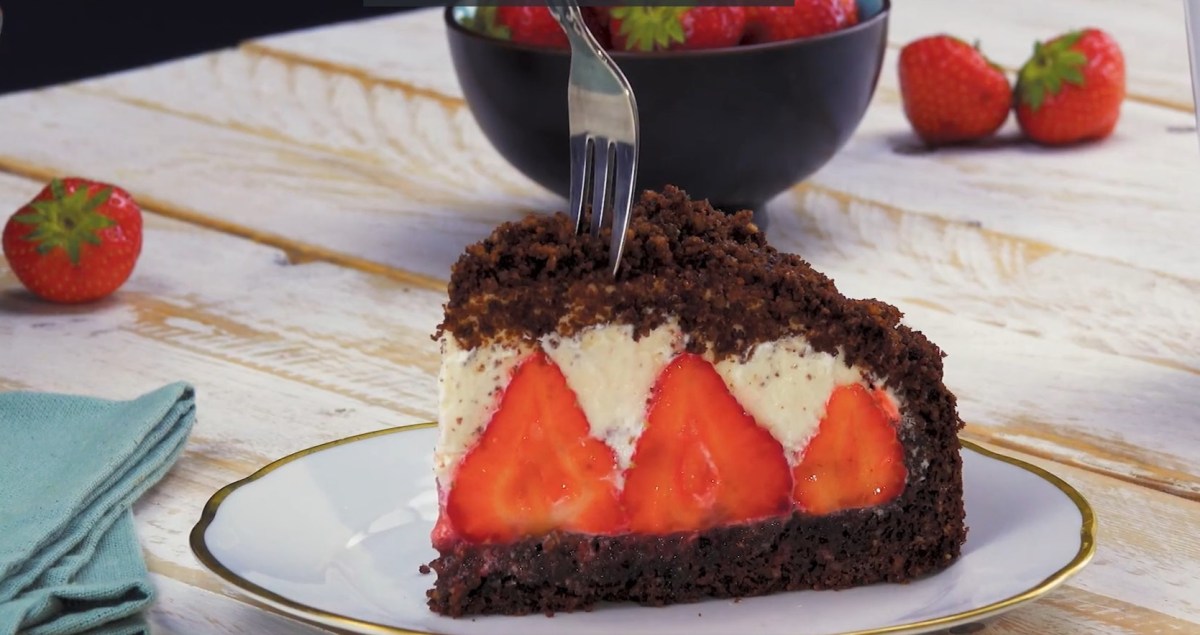 ein Stück Maulwurfkuchen mit Erdbeeren auf einem Teller, darin steckt eine Gabel.