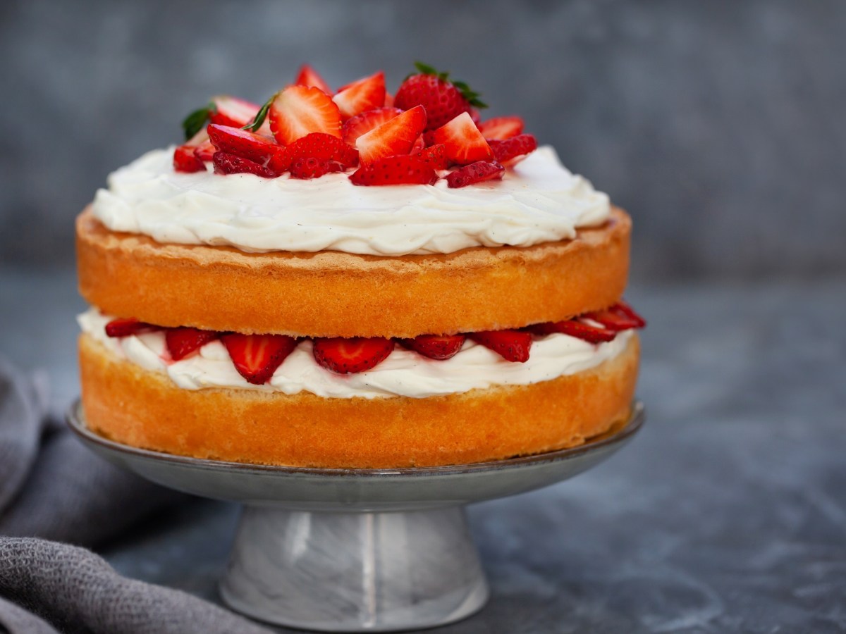 Ein Tortenständer mit Naked Cake mit Erdbeeren auf zwei Tortenböden und Sahne.