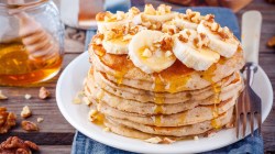 Pancakes auf einem weißen Teller mit Banane, Walnüssen und Sirup