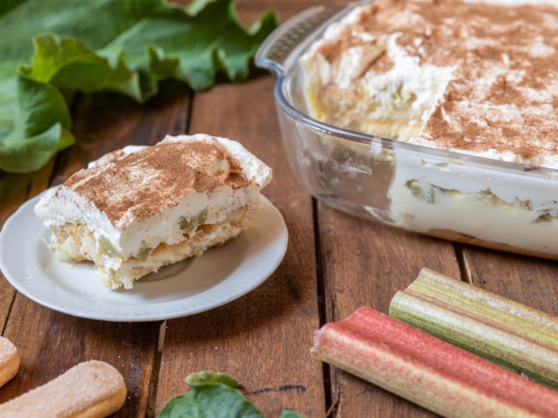 Eine Portion Rhabarber-Tiramisu auf einem Teller. Das restliche Dessert steht in einer Auflaufform dahinter.