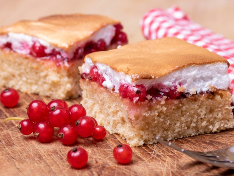 Zwei Stücke Ribiselkuchen. Daneben frische Johannisbeeren.