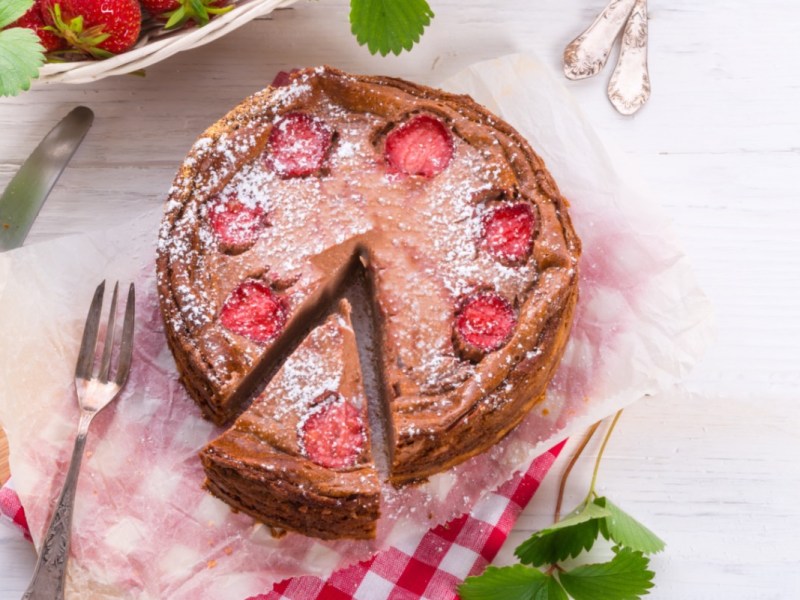 Ein Schoko-Käsekuchen mit Erdbeeren in der Draufsicht. Ein Stück wurde herausgeschnitten.