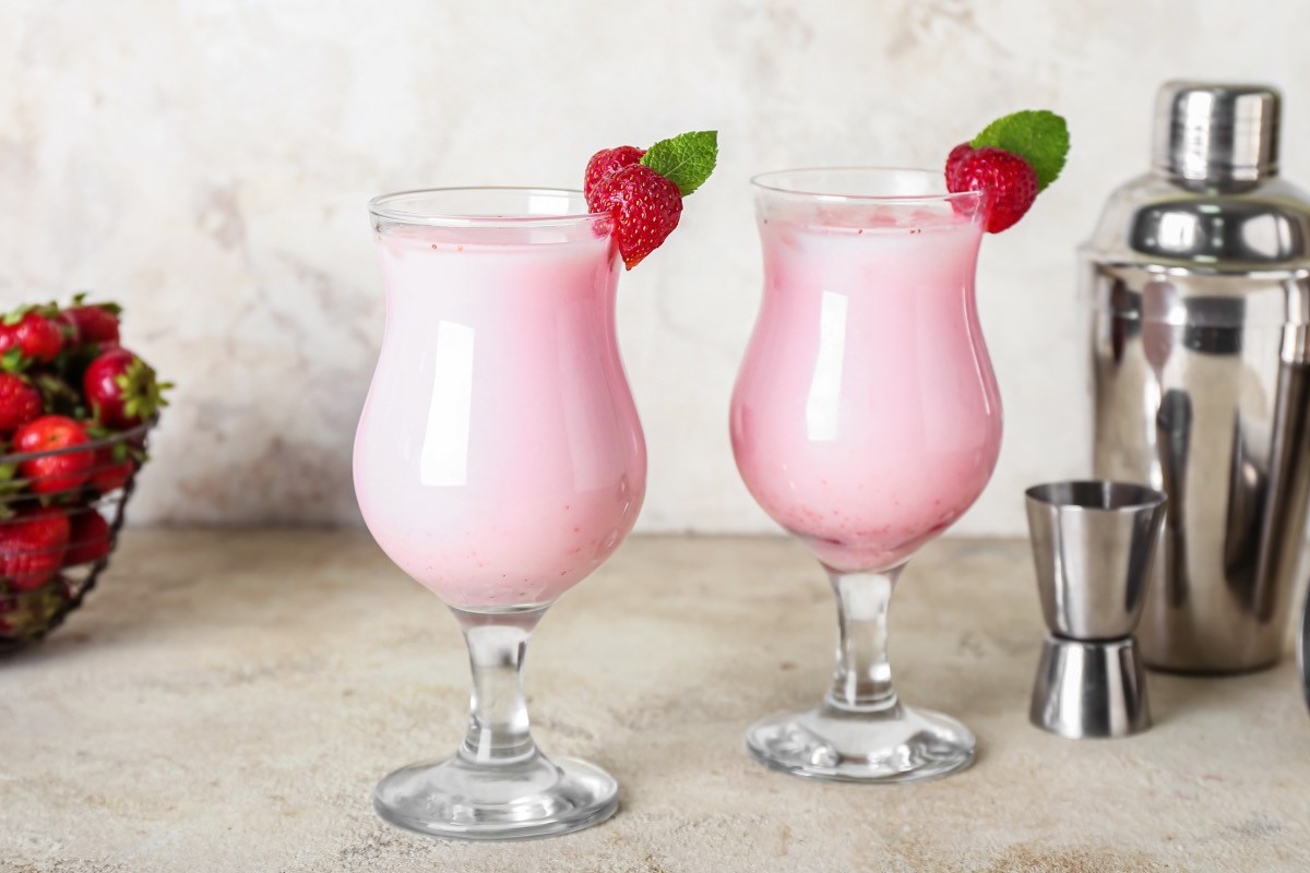 Zwei Gläser Strawberry Colada mit Erdbeeren als Deko. Daneben stehen Cocktailshaker.