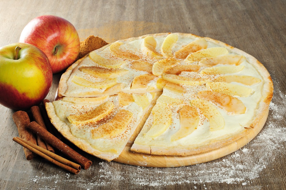 Apfel-Flammkuchen auf einem Tisch, Äpfel und Zimt daneben