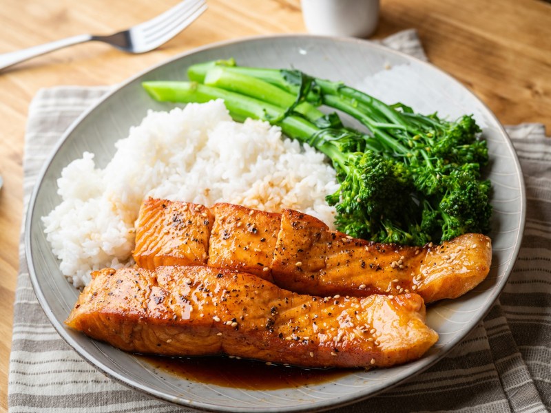 Teriyaki-Lachs mit Reis und Brokkoli serviert auf einem weißen Teller.