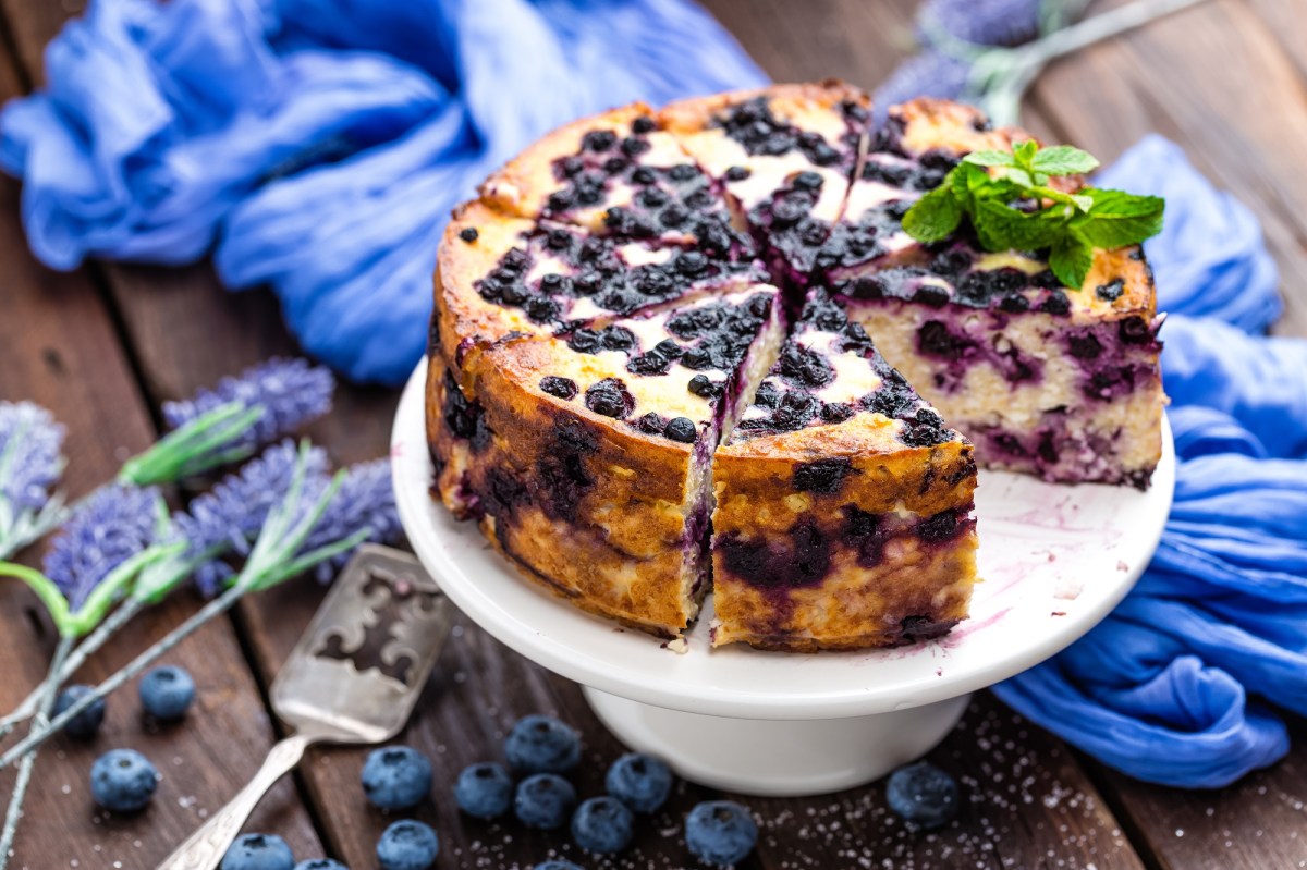 Eine angeschnittene Blaubeer-Joghurt-Torte auf einem dekorierten Tisch.