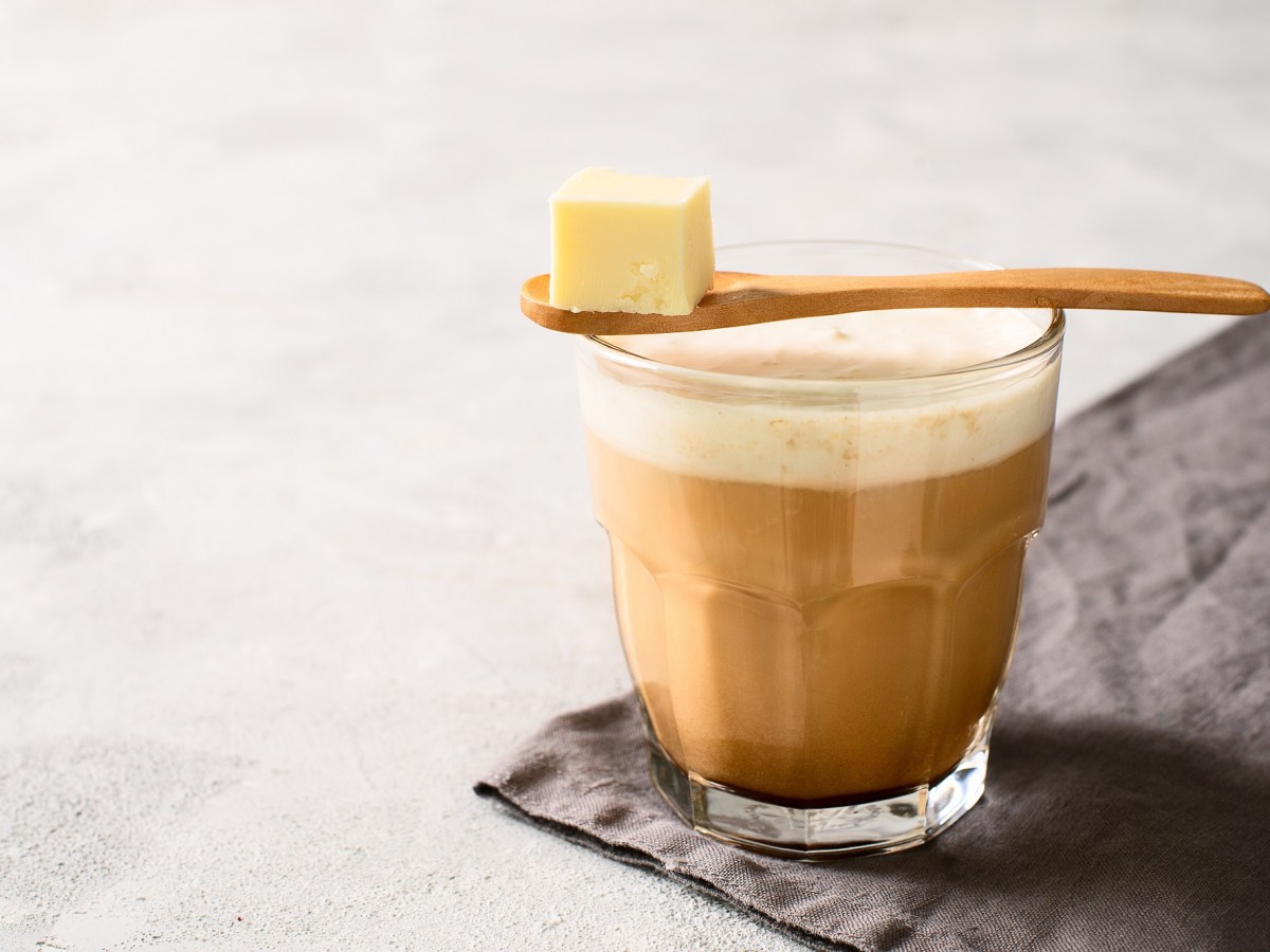 Bulletproof Coffee in einem Glas, darüber ein Löffel mit einem Stück Butter.