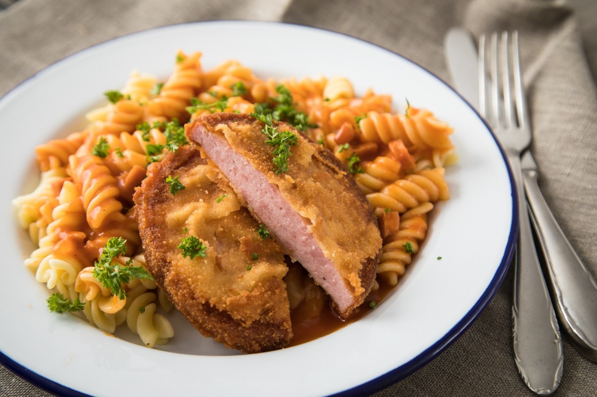 DDR-Rezepte: Jägerschnitel mit Spirellinudeln und Tomatensoße auf einem Teller, daneben Messer und Gabel, Nahaufnahme.