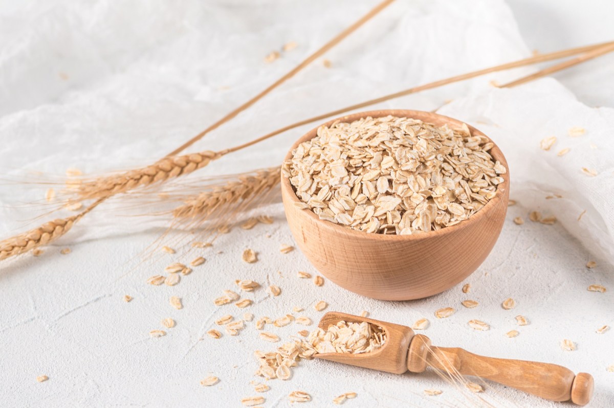 Haferflocken einweichen: eine Schale mit Haferflocken, daneben ein Holzlöffel und Hafer.