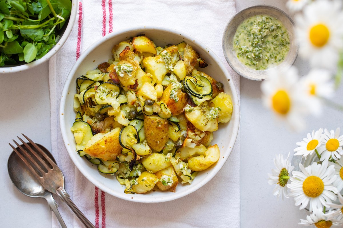 Kartoffelsalat mit gegrillter Zucchini in einer weißen Schale. Daneben steht eine Schale mit Dressing.