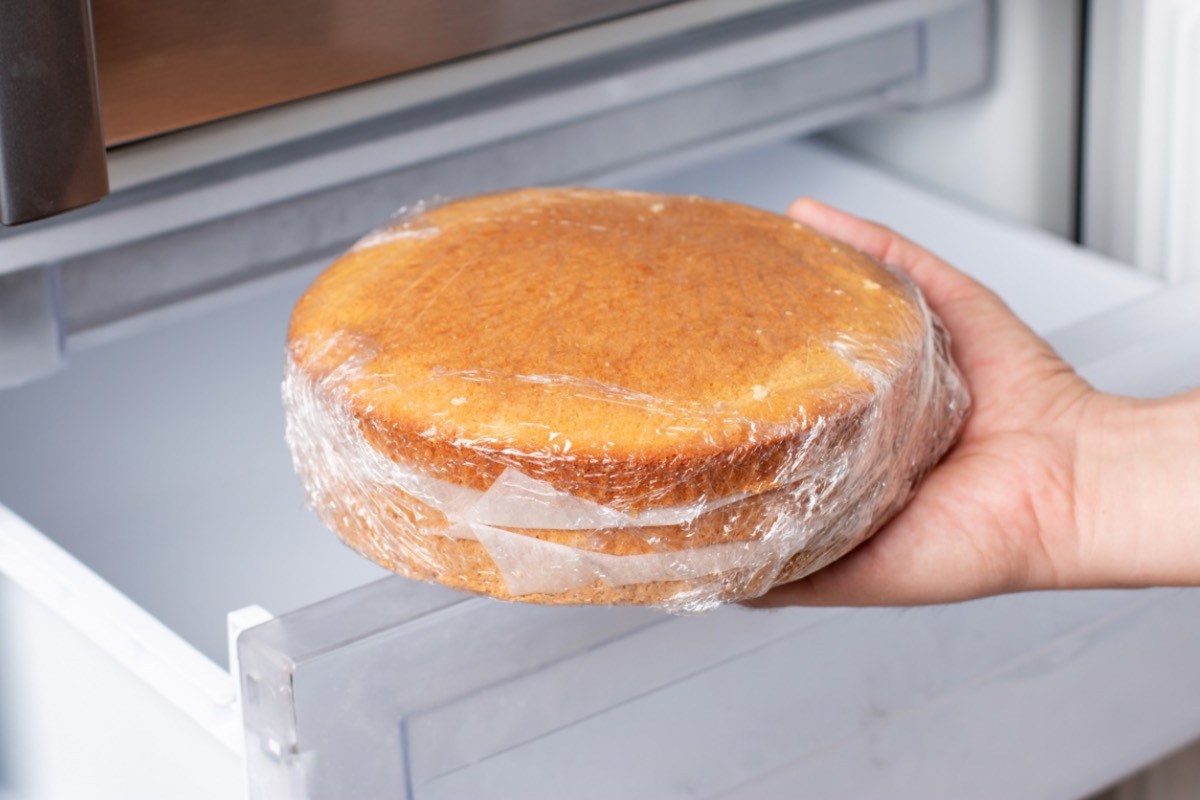 Kuchen aufbewahren und einfrieren: Ein in Frischhaltefolie gewickelter Kuchen wird in den Gefrierschrank gelegt.