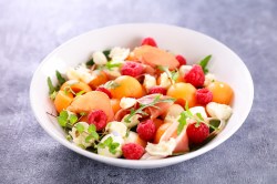 Melonensalat mit Schinken in einer weißen Schale.