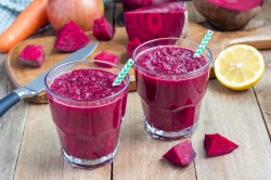 Zwei Gläser vom Rote-Bete-Apfel-Smoothie auf einem Holztisch.