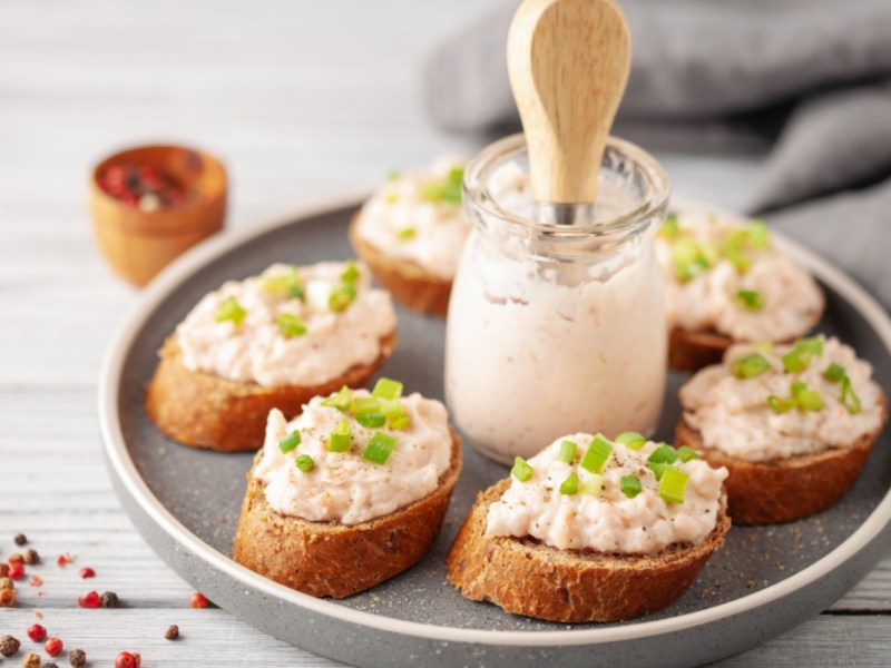 Thunfisch-Aufstrich auf mehreren Scheiben Baguette. In der Mitte steht ein Glas mit Aufstrich.