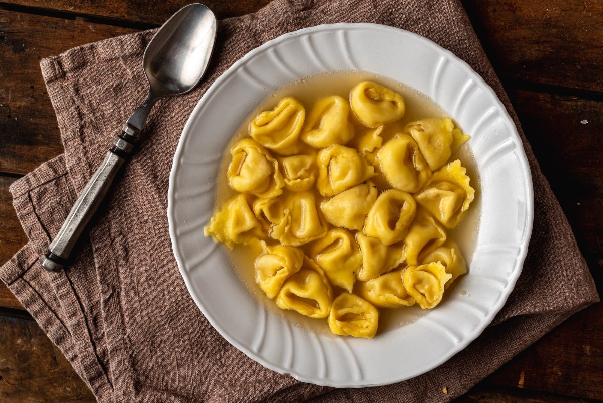 Tortellini in Brodo in einem weißen Teller. Daneben liegt ein Löffel.