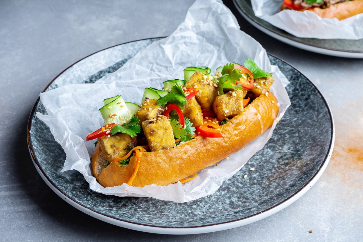 Ein Banh Mi Sandwich mit Tofu, Gurke, Paprika Koriander auf einem Teller.