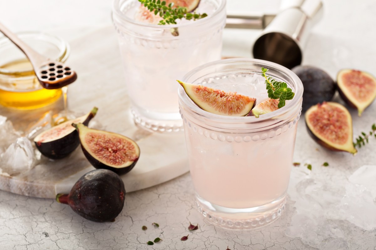 Ein Glas Feigen-Fizz garniert mit einem Stück Feige und Thymian, drumherum Zutaten wie frische Feigen.