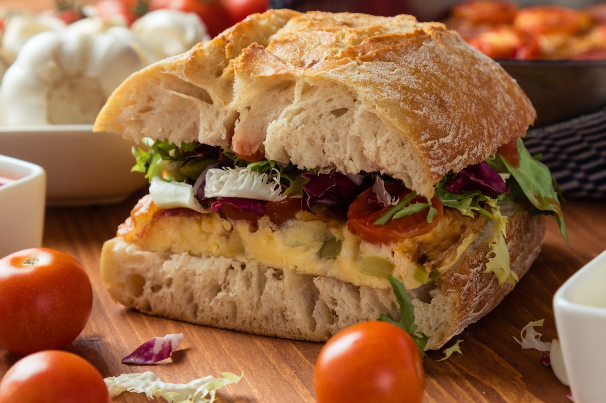 Frittata-Sandwich mit Salat, Tomate und Spinat, drumherum frische Zutaten, Nahaufnahme.